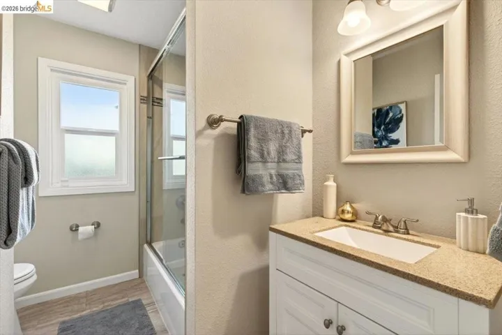 Full bathroom with vanity, bath / shower combo with glass door, and a textured wall