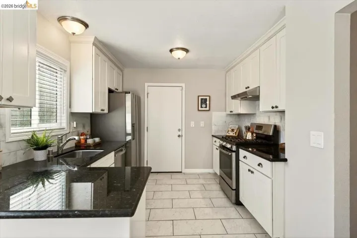 Kitchen featuring stainless steel appliances, white cabinets, dark stone counters, and backsplash