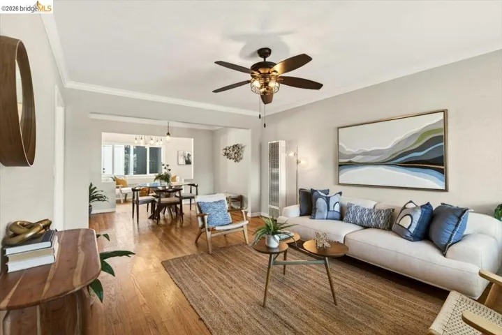 Living room featuring hardwood / wood-style flooring, a ceiling fan, a heating unit, crown molding, and hanging lights