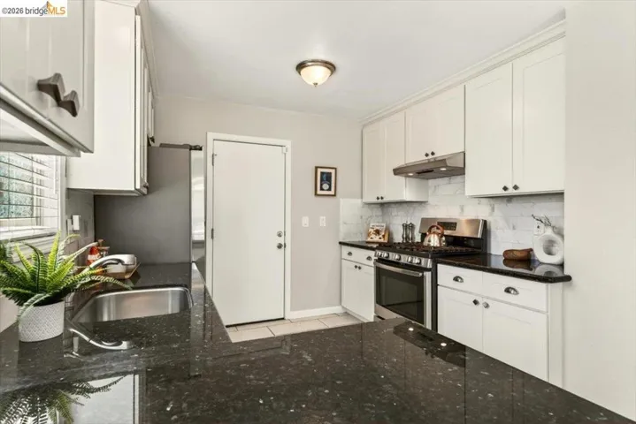 Kitchen with stainless steel appliances, dark stone counters, white cabinetry, and backsplash