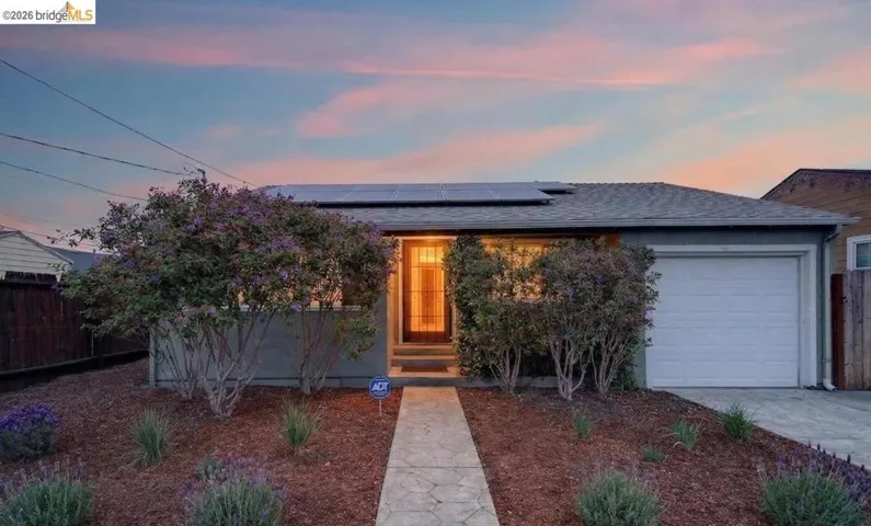 View of front of home featuring solar panels, an attached garage, a shingled roof, and concrete driveway