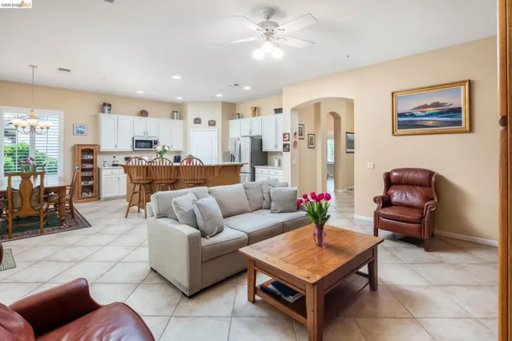 Living area featuring arched walkways, a ceiling fan, hanging lights, light tile patterned flooring, and plenty of natural light