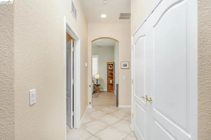 Hall with arched walkways, a textured wall, light tile patterned floors, and recessed lighting