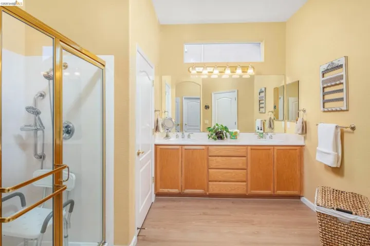 Full bath featuring double vanity, light wood-style floors, and a stall shower