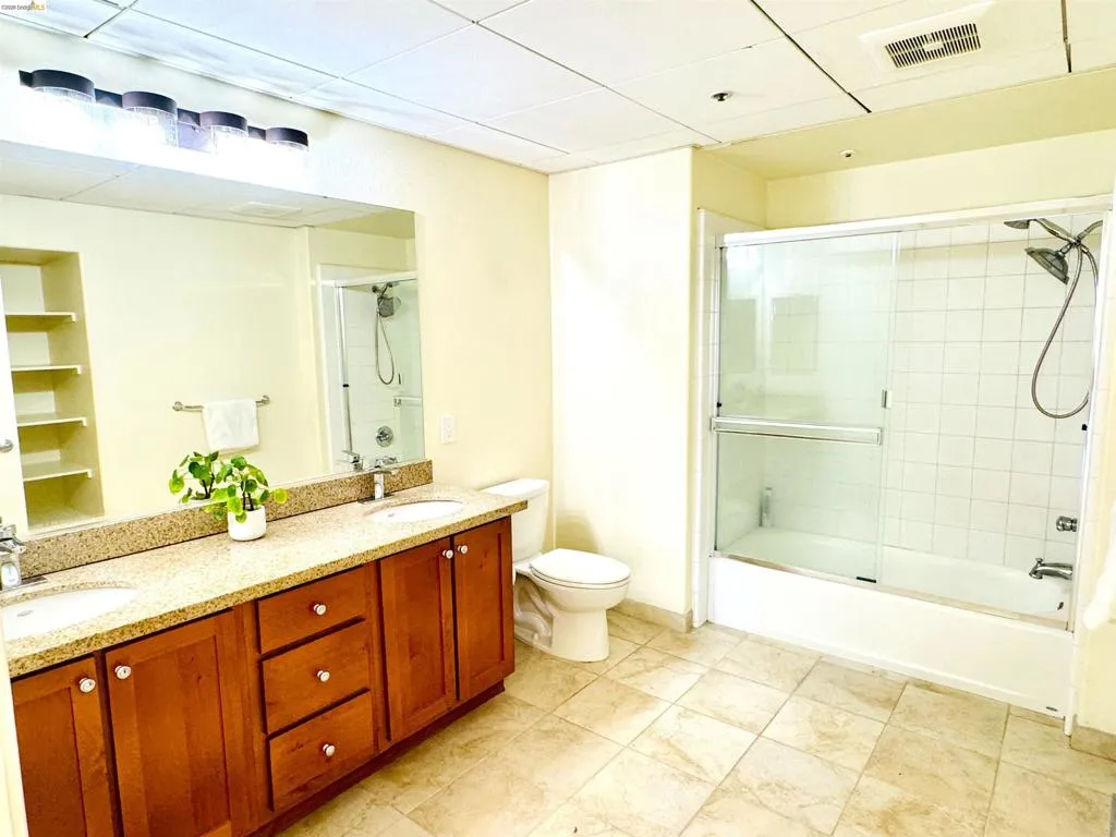 Full bathroom with double vanity, bath / shower combo with glass door, and a drop ceiling