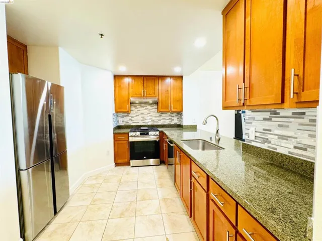 Kitchen with stainless steel appliances, dark stone counters, wood finish cabinets, recessed lighting, and light tile patterned floors