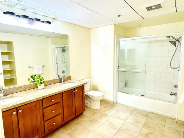 Full bathroom with double vanity, bath / shower combo with glass door, and a drop ceiling