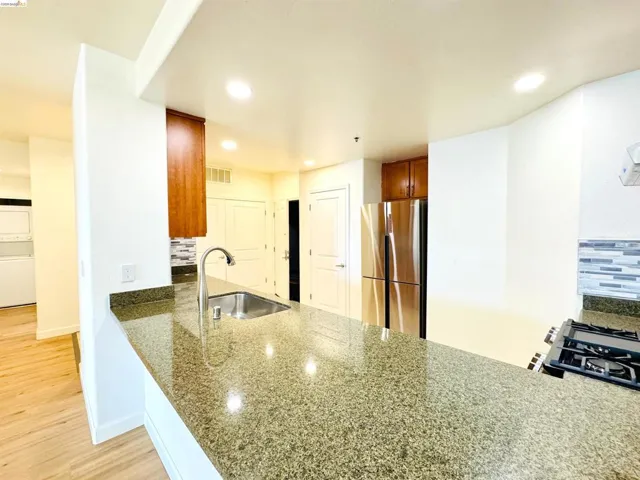 Kitchen featuring a peninsula, tasteful backsplash, freestanding refrigerator, light wood-type flooring, and dark stone countertops