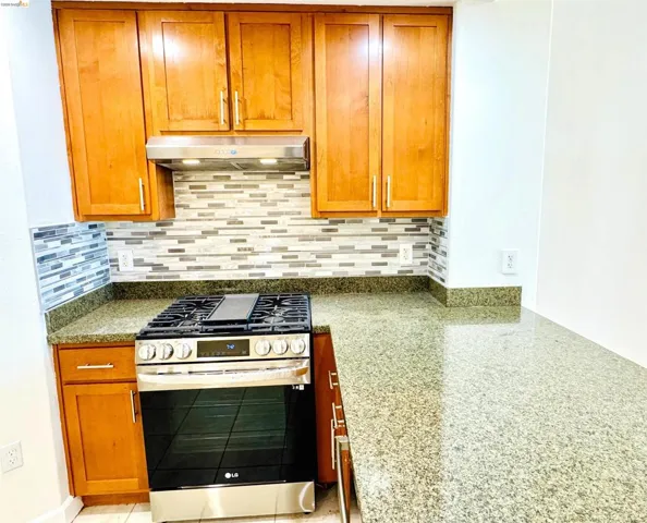 Kitchen with gas range, light stone countertops, wood finish cabinetry, and backsplash