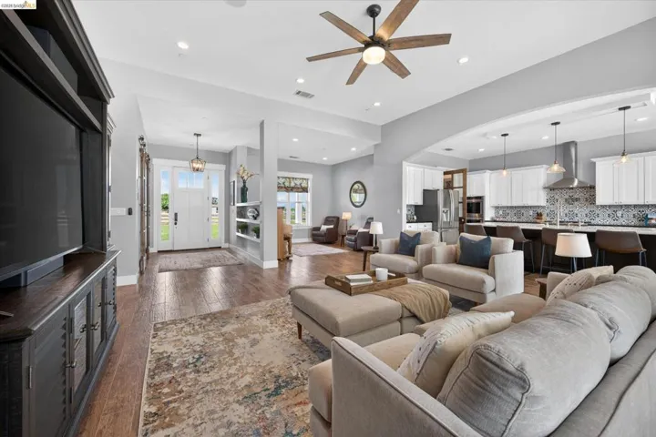 Living room with ceiling fan, dark wood-type flooring, recessed lighting, and arched walkways