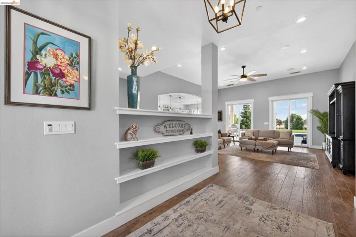 Living room featuring dark wood-style floors, suspended lighting, built in shelves, and a ceiling fan