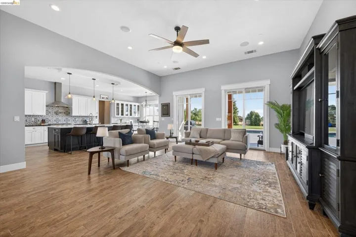 Living room featuring ceiling fan, dark wood finished floors, arched walkways, and suspended lighting