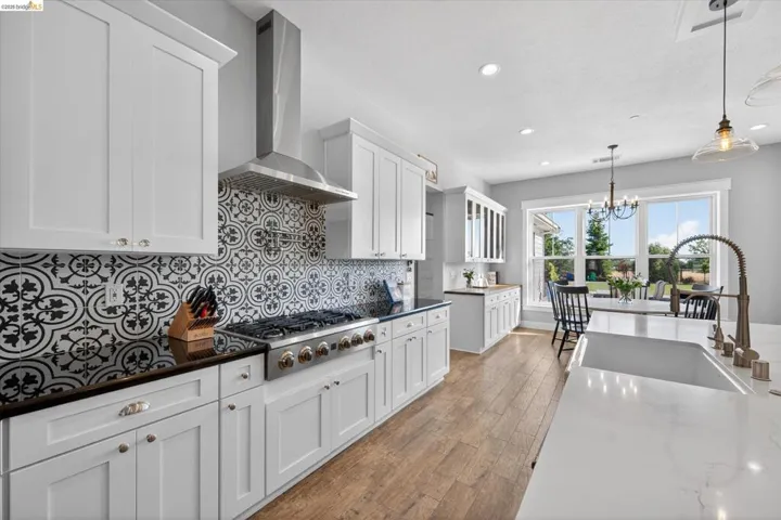 Kitchen featuring white cabinetry, dark stone counters, stainless steel gas cooktop, dark wood finished floors, and a chandelier
