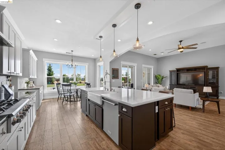 Kitchen with dark wood-type flooring, stainless steel appliances, light stone counters, a kitchen island with sink, and healthy amount of natural light