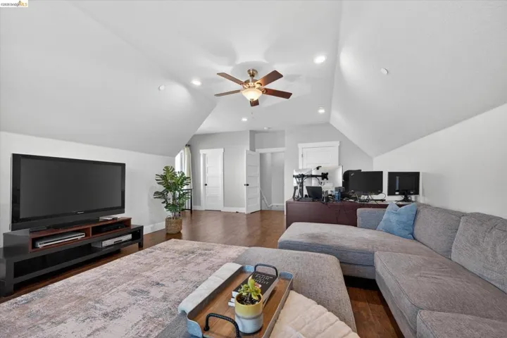 Living room featuring ceiling fan, dark wood-type flooring, vaulted ceiling, and a desk