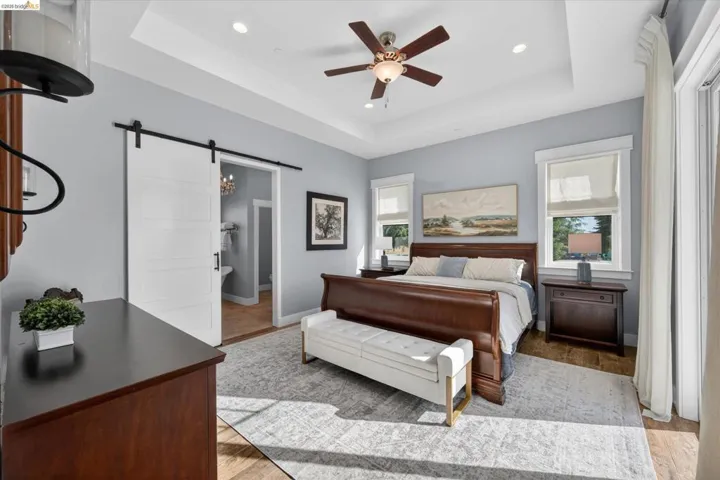 Bedroom featuring a barn door, a raised ceiling, recessed lighting, a ceiling fan, and light wood-type flooring