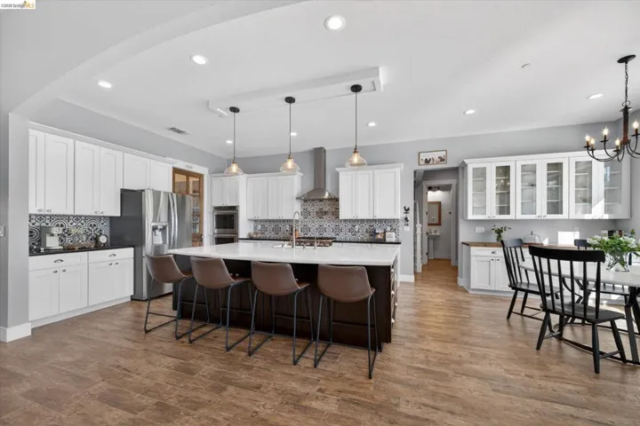 Two tone kitchen featuring a breakfast bar, a kitchen island with sink, dual tone cabinets, stainless steel appliances, and glass insert cabinets