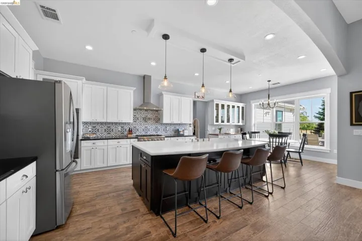 Kitchen featuring stainless steel fridge, a breakfast bar area, a center island with sink, dark wood-type flooring, and dual tone cabinets