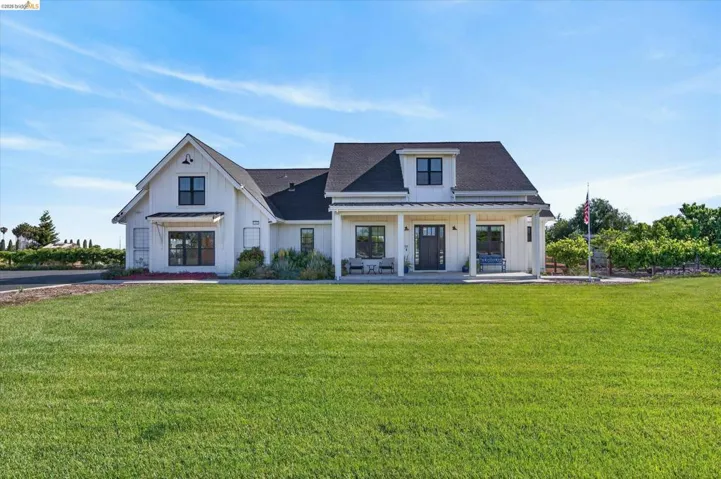 Modern farmhouse featuring board and batten siding, a standing seam roof, a front yard, a shingled roof, and a porch
