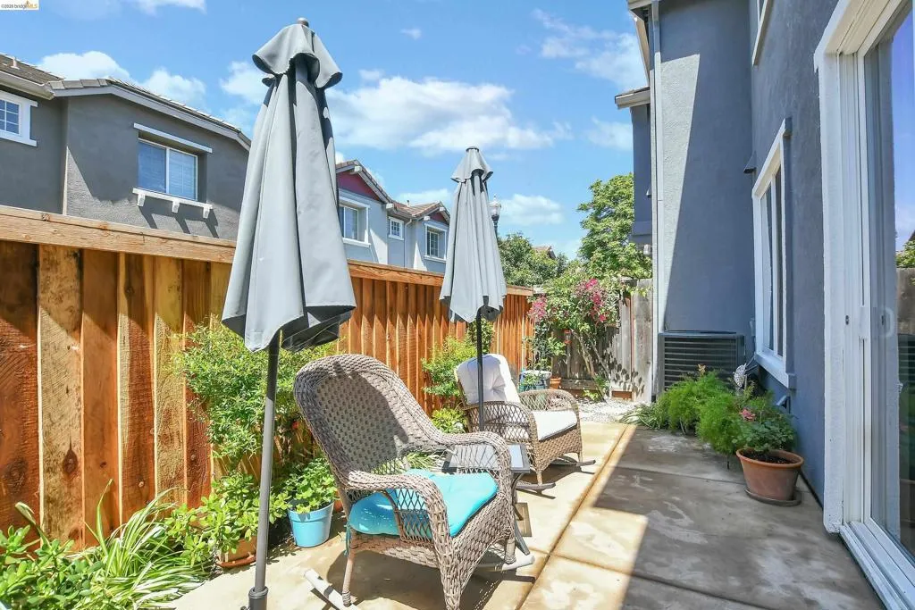 Paved patio area featuring a wooden privacy fence, mature perimeter landscaping, and a sliding glass door entry to the interior