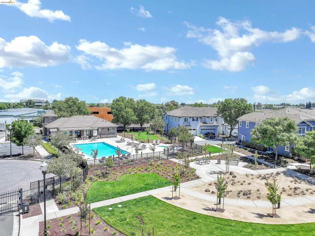 Community amenities featuring a swimming pool, paved sundeck with lounge chairs, a clubhouse with a covered patio, and a landscaped recreational area with walking​​‌​​​​‌​​‌‌​​‌​​​‌‌​​​‌​​‌‌​​‌‌​​‌‌​​​​ paths