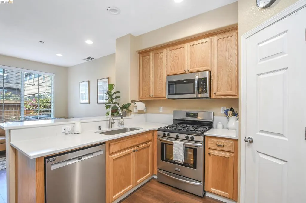 Kitchen featuring wood cabinetry, stainless steel appliances, a gas range, a single basin sink, and light-toned countertops