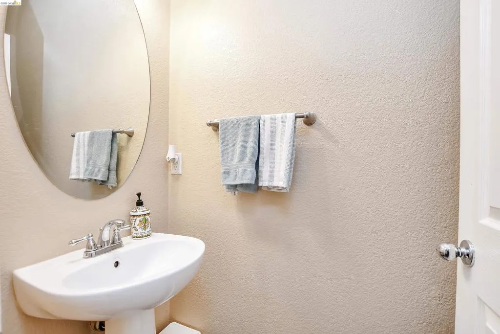 Pedestal sink with chrome faucet, complemented by an oval wall-mounted mirror