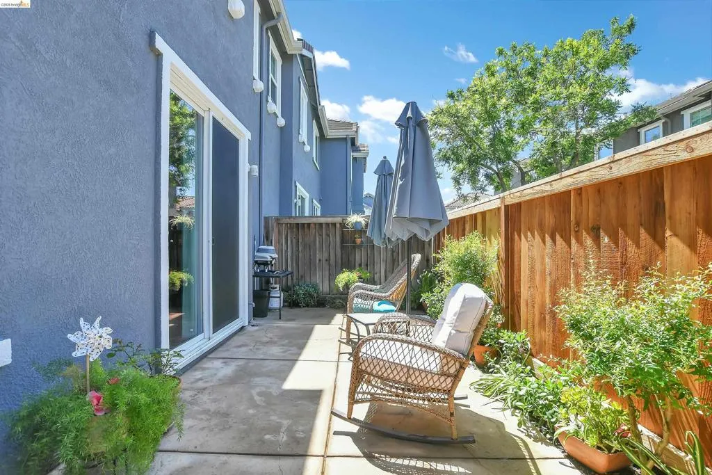 Paved patio area featuring a sliding glass door, privacy fencing, and surrounding plantings