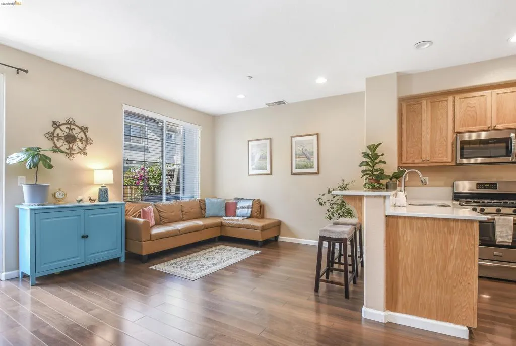 Open-concept living space featuring wood-finish flooring, a sliding glass door, recessed lighting, and a kitchen with stainless steel appliances, wood cabinetry, and a peninsula with seating