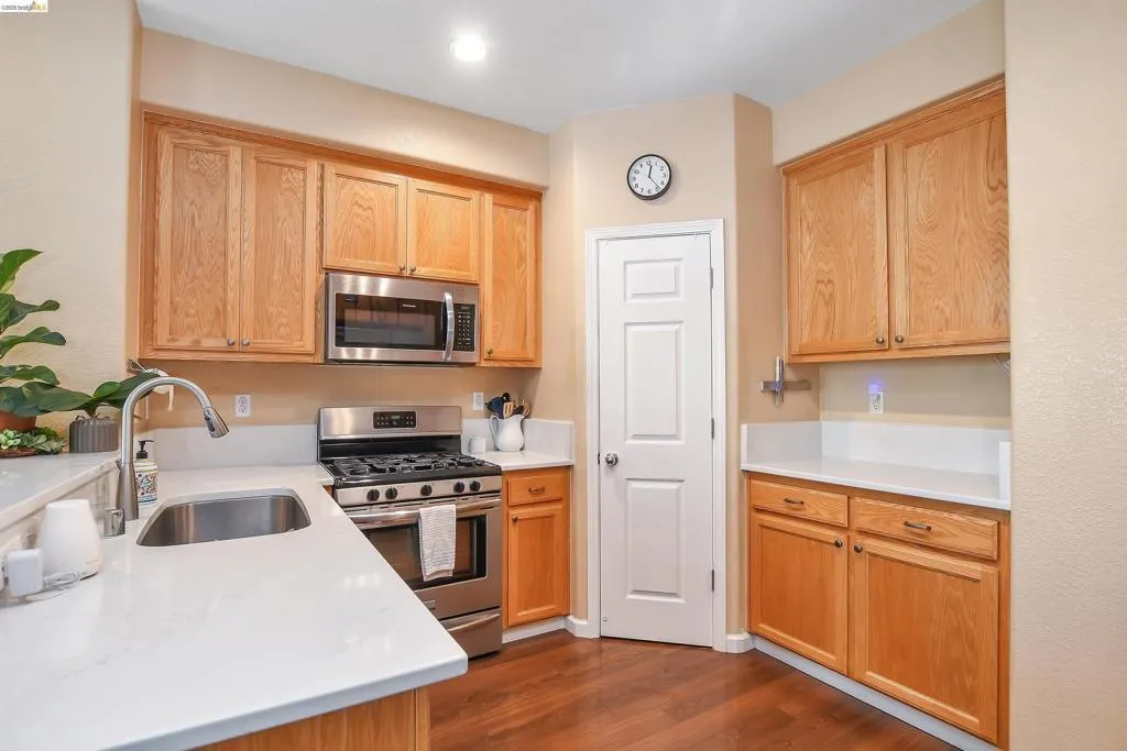 Kitchen featuring light wood cabinetry, stainless steel appliances, white countertops, and wood-finish flooring