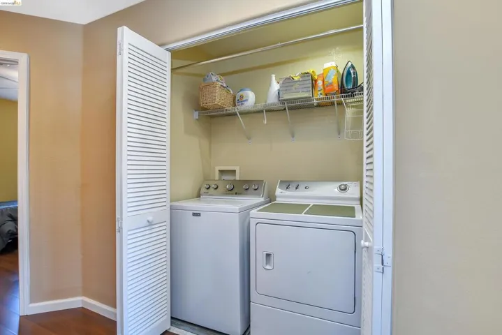 Dedicated laundry closet featuring a washer, dryer, bi-fold louvered doors, and elevated wire shelving