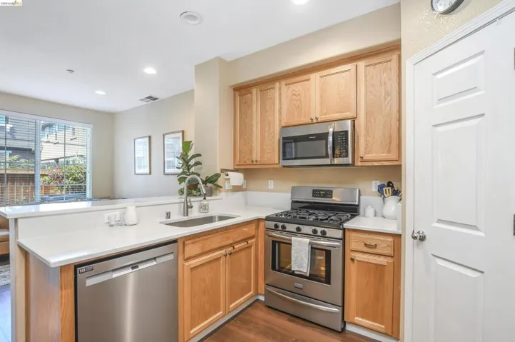 Kitchen featuring wood cabinetry, stainless steel appliances, a gas range, a single basin sink, and light-toned countertops