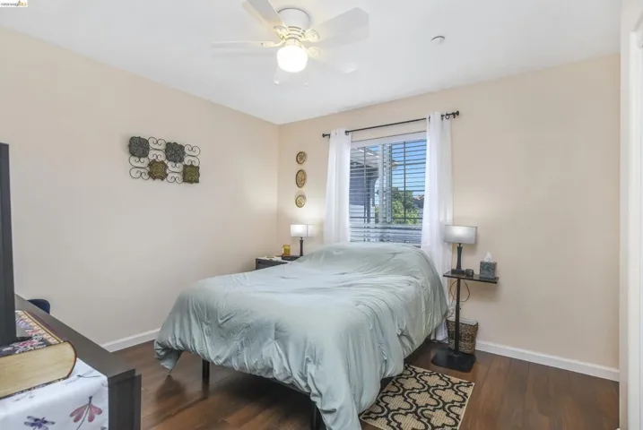 Bedroom featuring wood-finish flooring, a ceiling fan with integrated lighting, and a window with horizontal blinds and sheer white curtains
