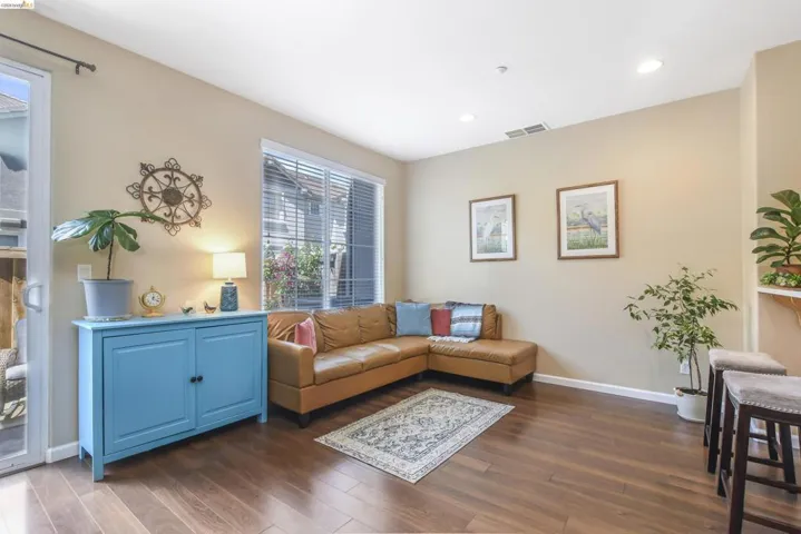Spacious living area featuring wood-finish flooring, recessed lighting, a large window with horizontal blinds, and a sliding glass door providing access to exterior space