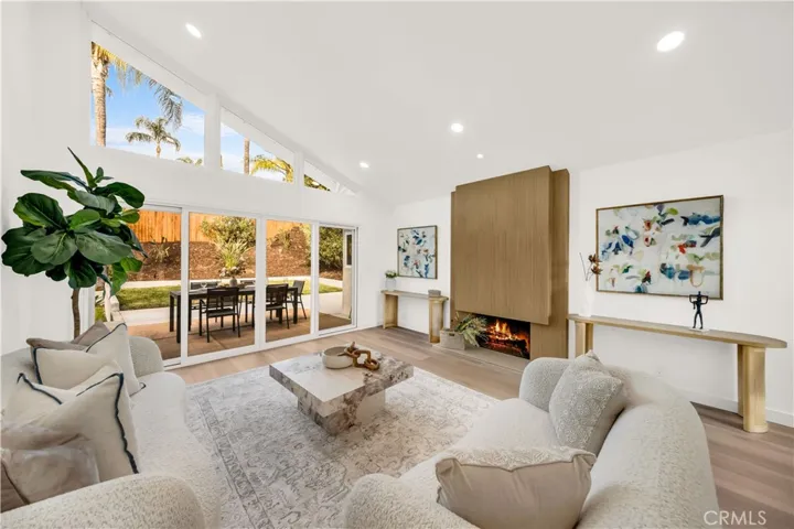 Spacious and airy living room with vaulted ceilings, large windows bringing in natural light, and a cozy fireplace, seamlessly connecting to the backyard patio.