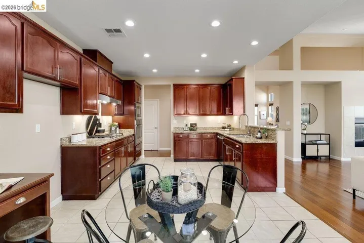 Kitchen featuring light tile patterned floors, light stone counters, a peninsula, recessed lighting, and bold wood finish cabinetry