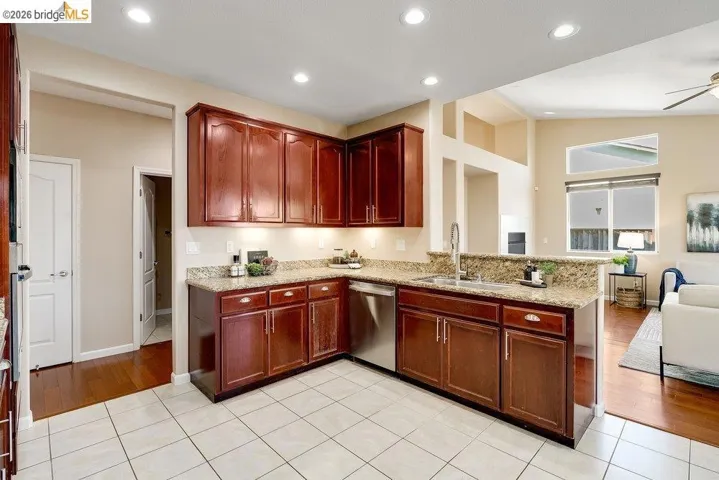 Kitchen with light tile patterned floors, light stone counters, open floor plan, dishwasher, and reddish brown cabinets