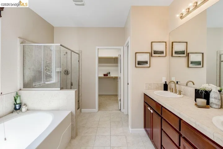 Full bath featuring double vanity, a bath, a shower stall, a walk in closet, and light tile patterned floors