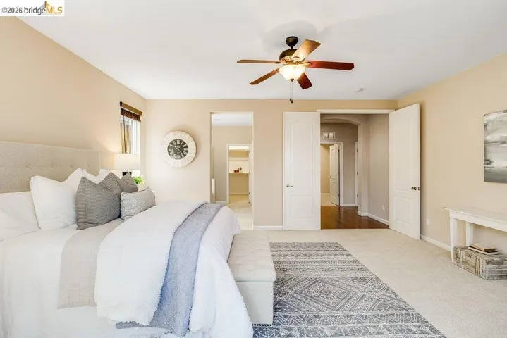 Carpeted bedroom featuring ensuite bathroom, a ceiling fan, and arched walkways