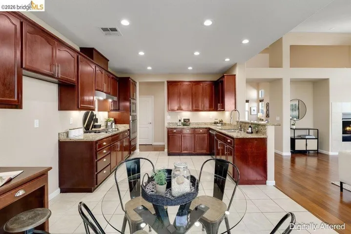 Kitchen with light tile patterned flooring, light stone countertops, a peninsula, a fireplace, and recessed lighting