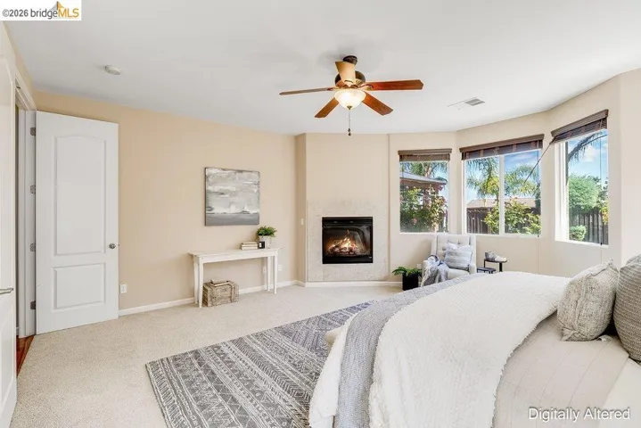 Bedroom featuring light colored carpet, a glass covered fireplace, and a ceiling fan