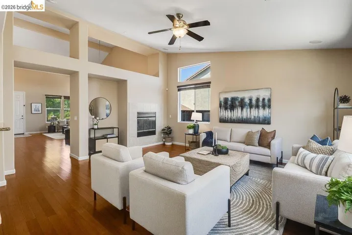 Living room with wood finished floors, a ceiling fan, vaulted ceiling, and a tiled fireplace