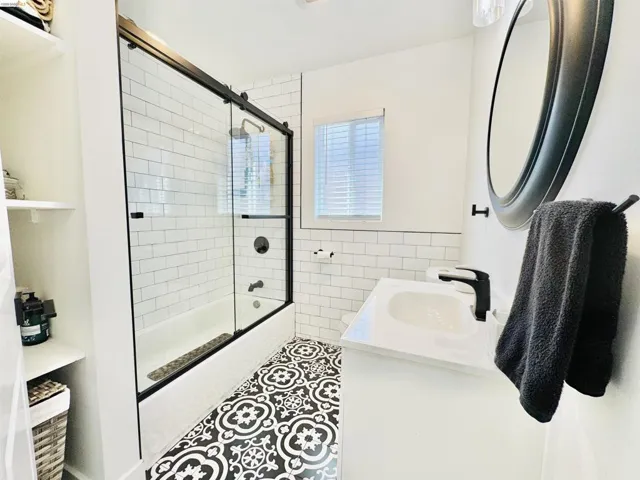 Bathroom featuring tile walls, combined bath / shower with glass door, vanity, and tile patterned flooring
