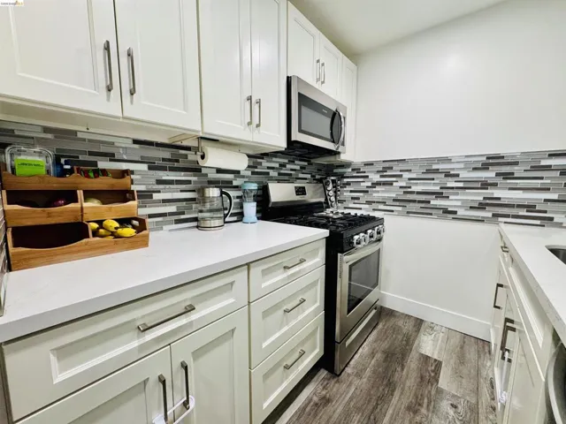 Kitchen with stainless steel appliances, white cabinetry, dark wood-style flooring, and light stone counters