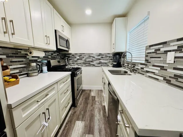 Kitchen with stainless steel appliances, light stone counters, white cabinets, dark wood finished floors, and recessed lighting