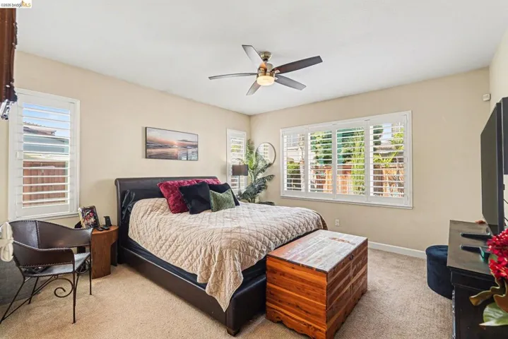 Bedroom with light colored carpet, multiple windows, and a ceiling fan