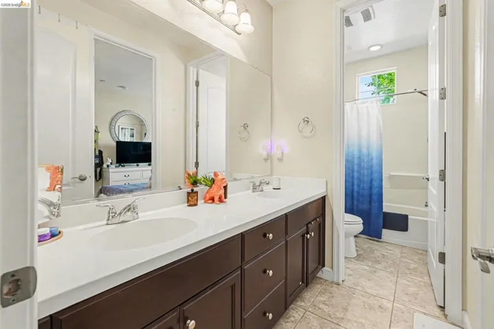 Bathroom with double vanity, shower / tub combo with curtain, light tile patterned floors, and connected bathroom