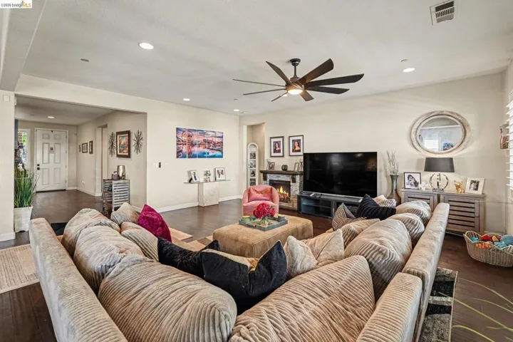 Living area with a lit fireplace, dark wood-type flooring, ceiling fan, and recessed lighting