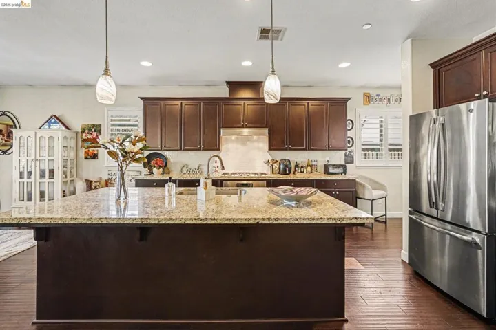 Kitchen featuring dark wood finish cabinetry, stainless steel appliances, a kitchen bar, light stone countertops, and a kitchen island with sink