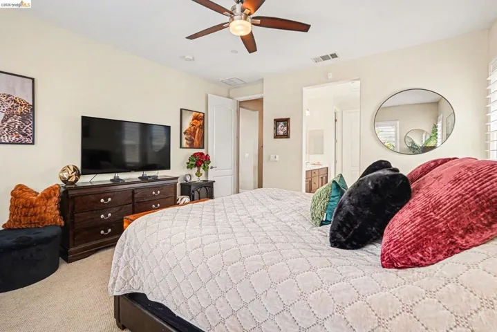 Bedroom with ceiling fan, light colored carpet, and connected bathroom